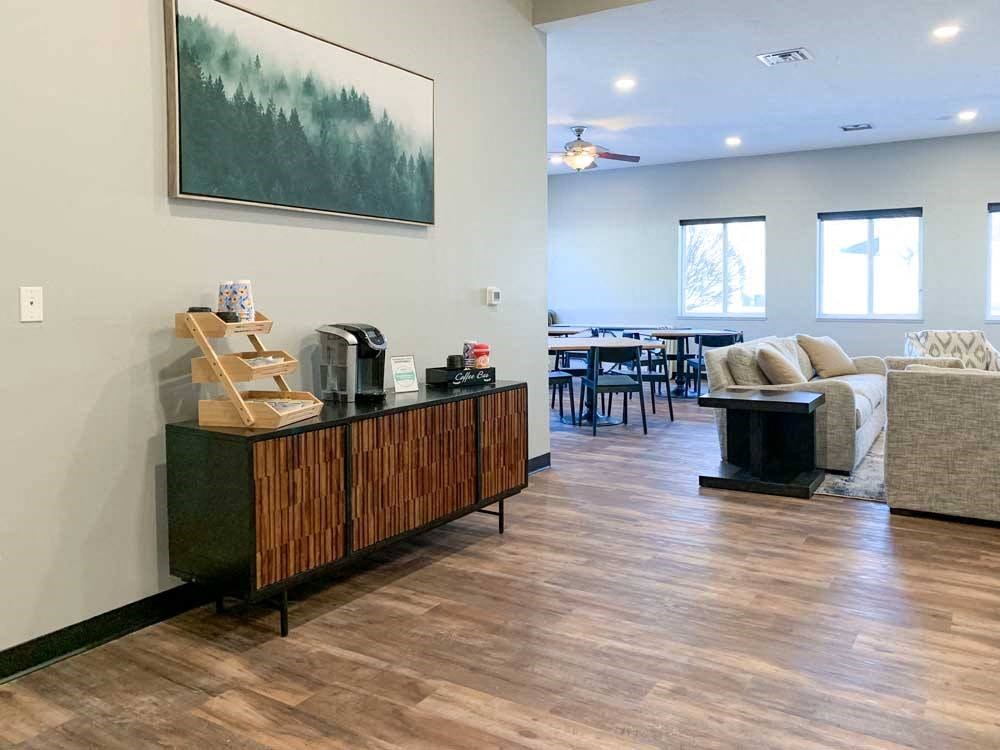 a clubhouse kitchen and tv lounge with wooden floors and furniture, a painting on the wall, and a wooden cabinet with items on top
