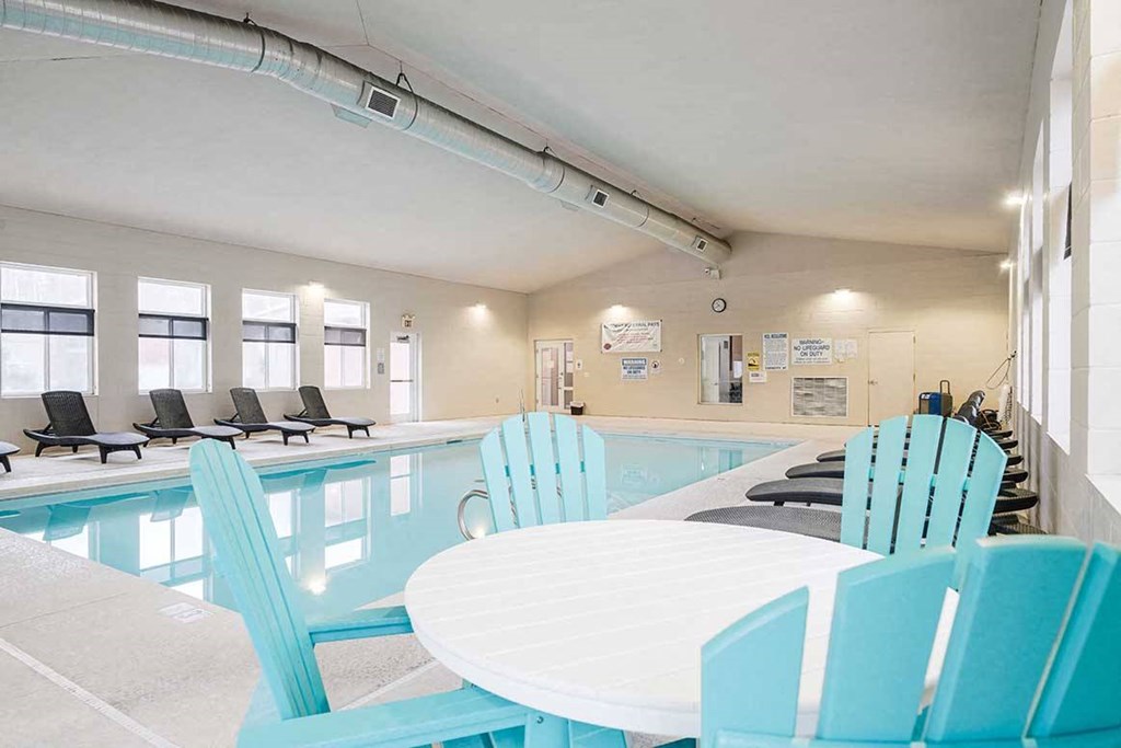 an indoor swimming pool with lounge chairs and a nearby table