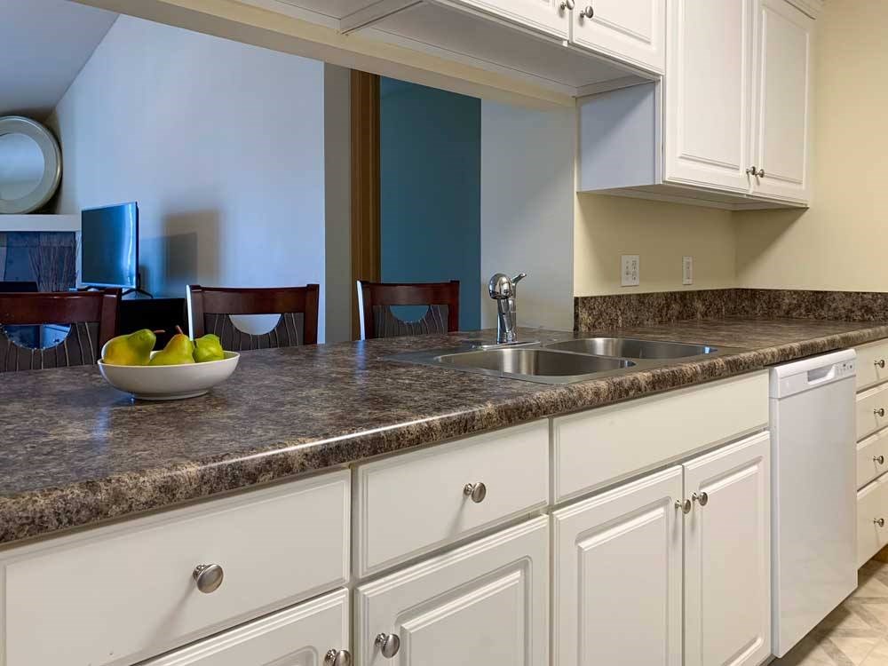 a kitchen with white cabinets and a grey countertop, with a window to the living room