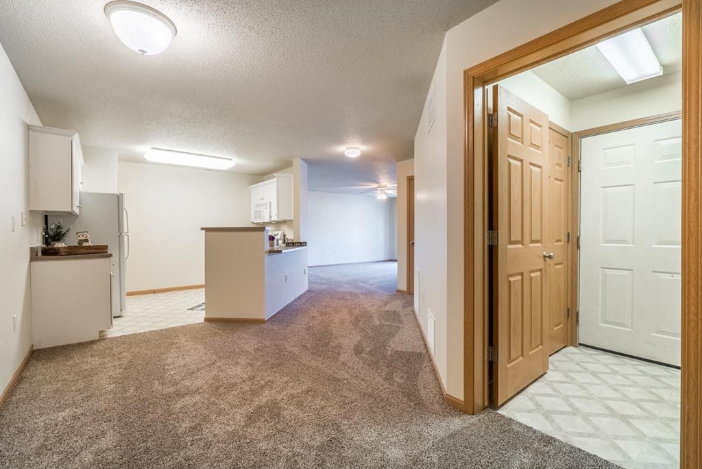 A kitchen with white cabinets and a refrigerator is visible through an open door.