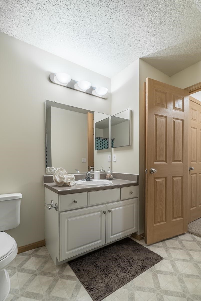 A bathroom with a white toilet, a sink with a mirror above it, and a brown door.