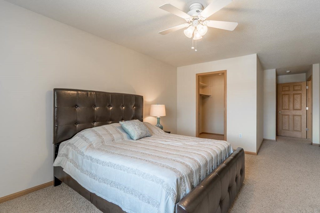 A bedroom with a bed, a ceiling fan, and a lamp.