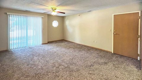 a living room with a ceiling fan, carpeted floor, a sliding glass door with vertical blinds