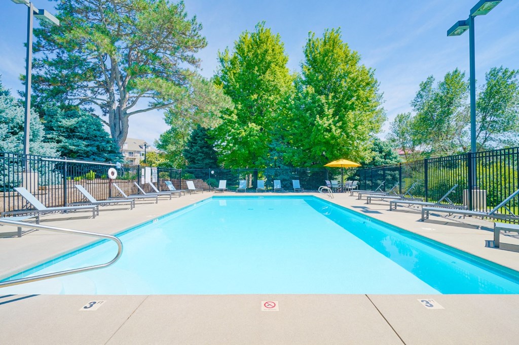 Swimming pool with lounge chairs for sunbathing and table shaded by yellow umbrella in the back