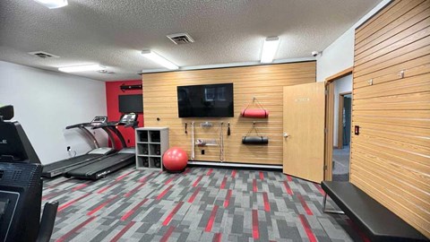 a 24-hour fitness center with treadmills, TVs, yoga equipment, and wooden paneling on the walls