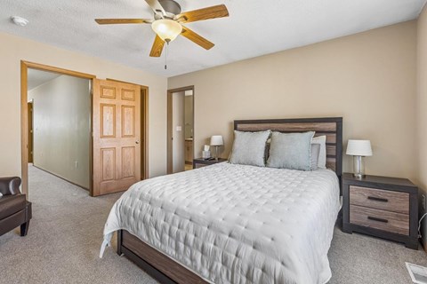 A bedroom with a large bed, a ceiling fan, and a nightstand with a lamp.