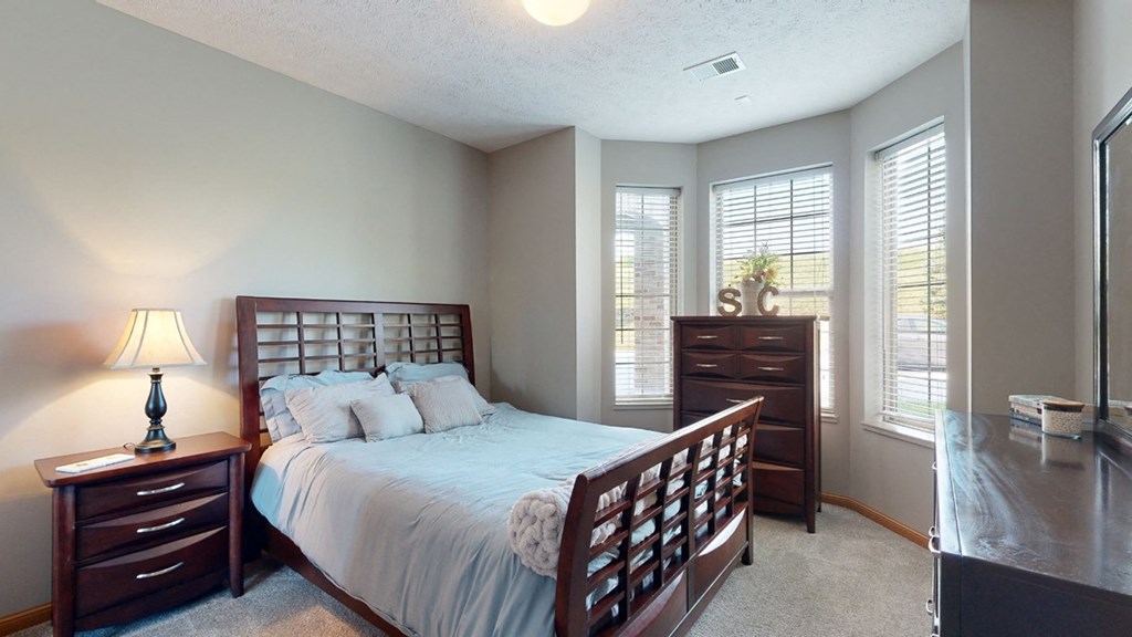 a bedroom with a bed and a dresser brightened with natural light from windows