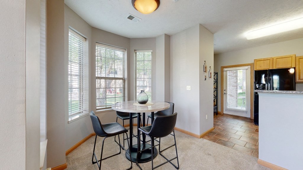 a dining area with a table and chairs and a kitchen in the background