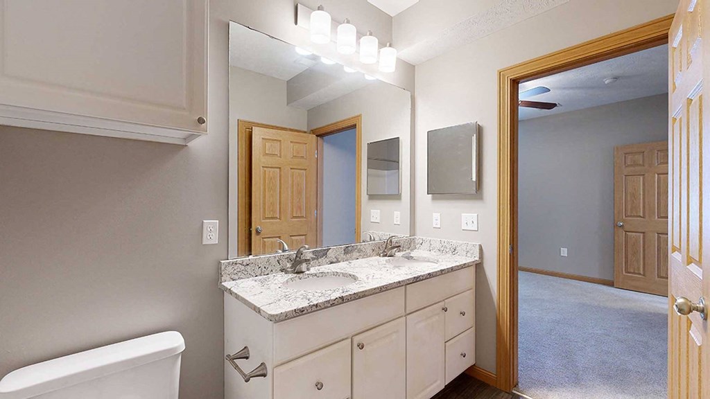 a bathroom with a vanity sink with granite counter top and a mirror with overhead lighting