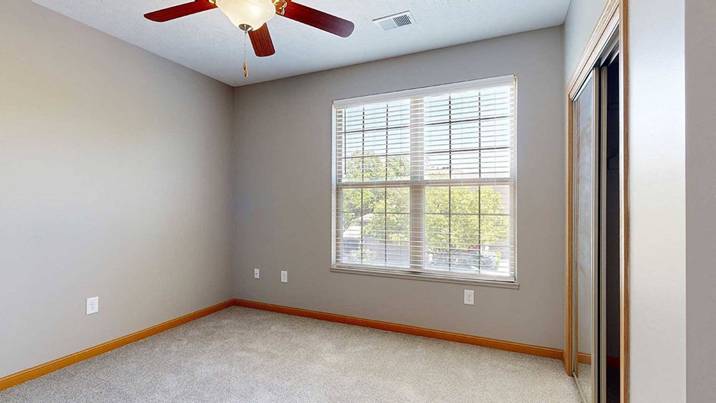 a bedroom with a large window, a ceiling fan, and a sliding door closet
