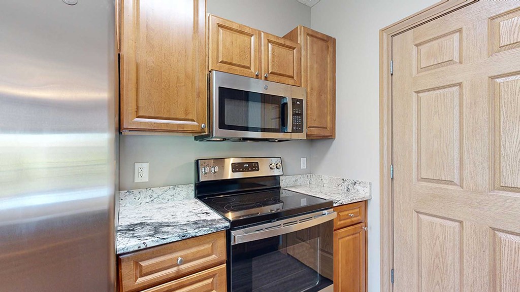 a kitchen with a stove and microwave and wooden cabinets and a granite countertop
