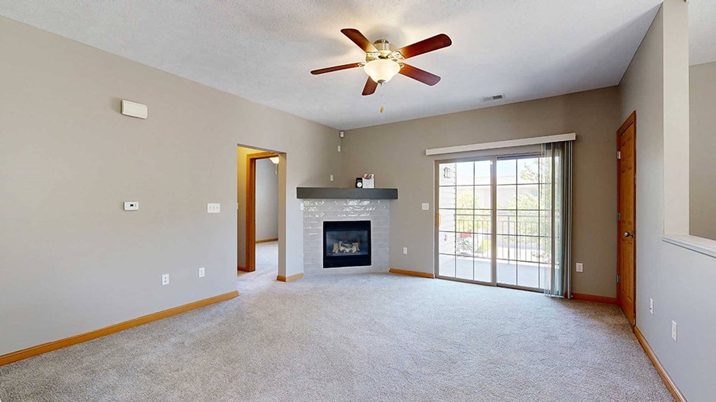 a living room with a fireplace, sliding glass doors to a balcony, and a ceiling fan