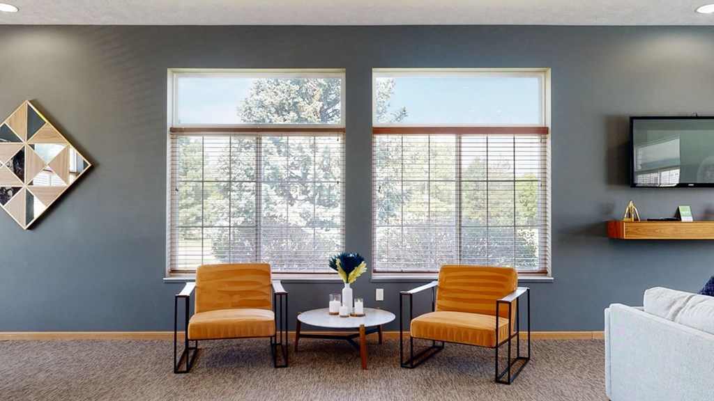 clubhouse living room with two orange chairs and a white coffee table in front of two large windows