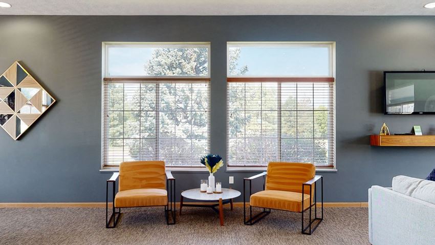 Stone-Ridge-Estates-Clubhouse-Amenities-Lincoln-NE-25 clubhouse living room with two orange chairs and a white coffee table in front of two large windows