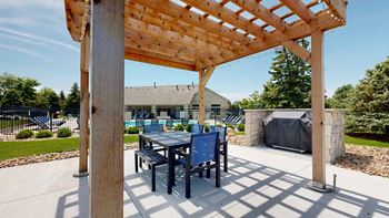 a wooden pergola with a table and chairs underneath it next to a grill