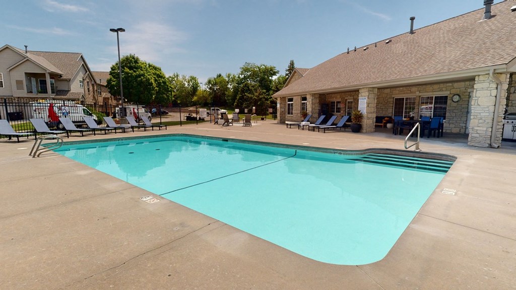 a swimming pool with lounge chairs and the clubhouse building in the background