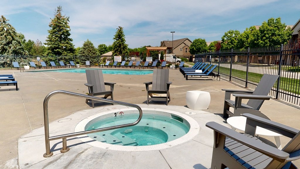 a hot tub with chairs around it and pool and trees in the background