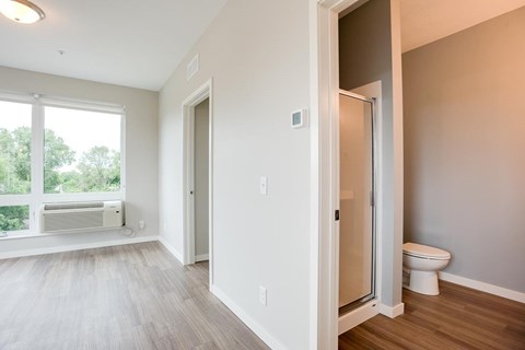 View looking into bathroom with standup shower and toilet and living room with large window