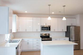 A large L-shaped kitchen with an island. cabinets and counters are white with stainless steel appliances