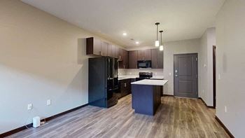 an open-concept living room and kitchen with dark cabinets and black appliances