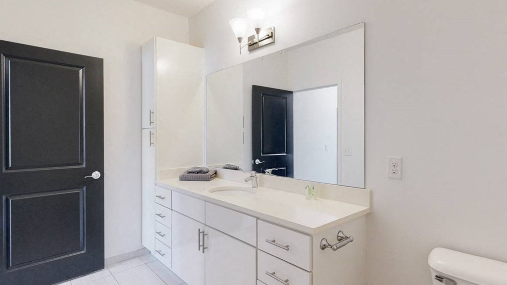 Furnished apartment bathroom with large white vanity and left side storage cabinet