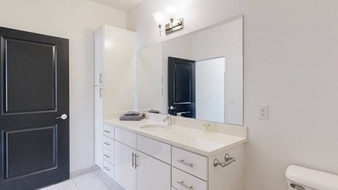 Furnished apartment bathroom with large white vanity and left side storage cabinet