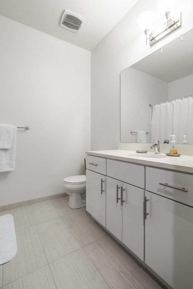 Contemporary bathroom with white cabinetry and white quartz countertops at The Conrad apartments