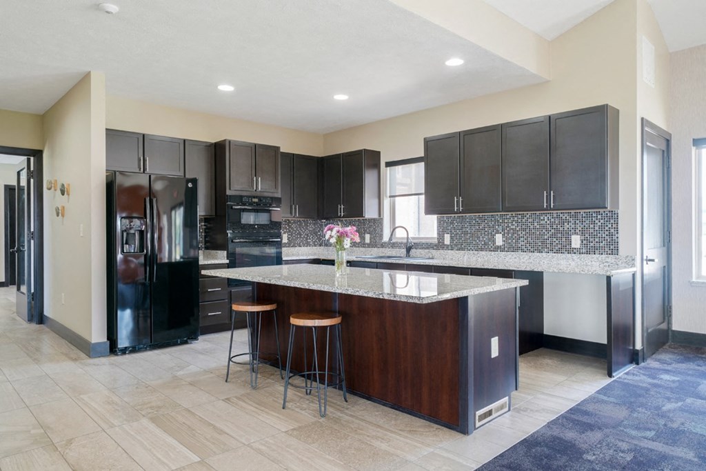 the large community kitchen with dark cabinets and a large island with a granite countertop