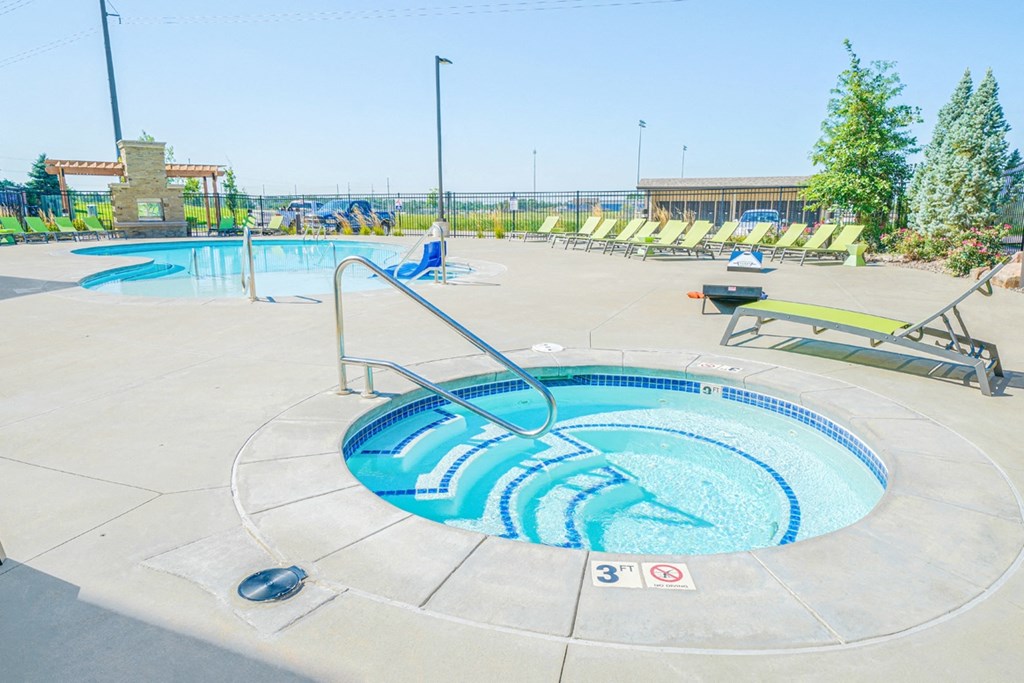 a hot tub with green lounge chairs and trees in the background