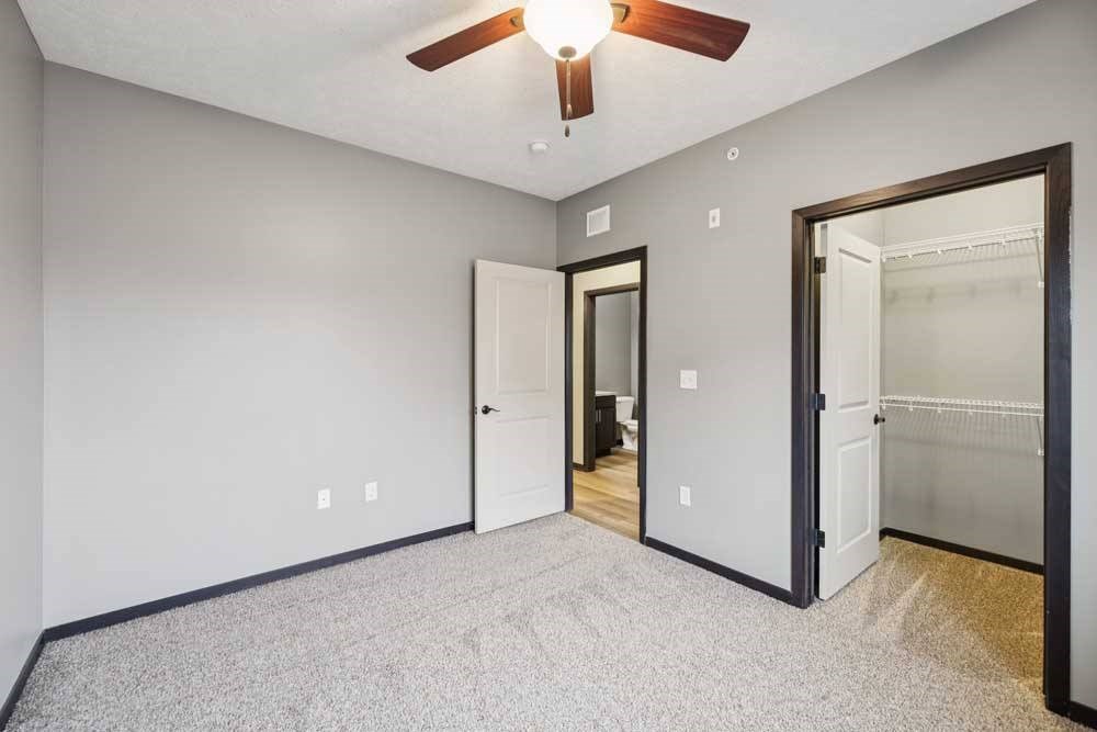 A carpeted bedroom with a walk-in closet and a ceiling fan.
