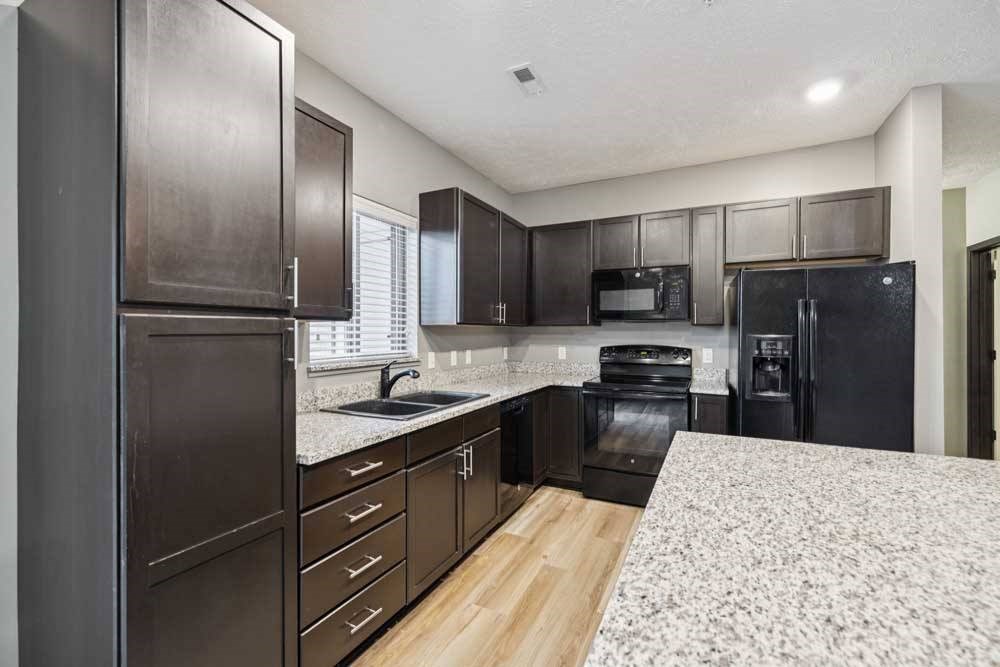 A kitchen with dark cabinets, granite counters, and black appliances.