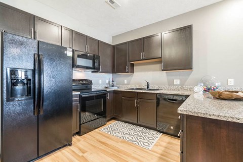 A kitchen with a black refrigerator and brown cabinets.