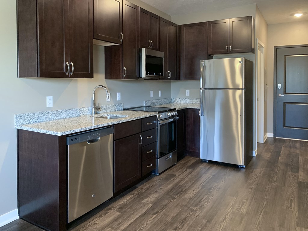 Kitchen with dark brown cabinets and matching stainless steel appliances in a studio apartment at the flats at shadow creek