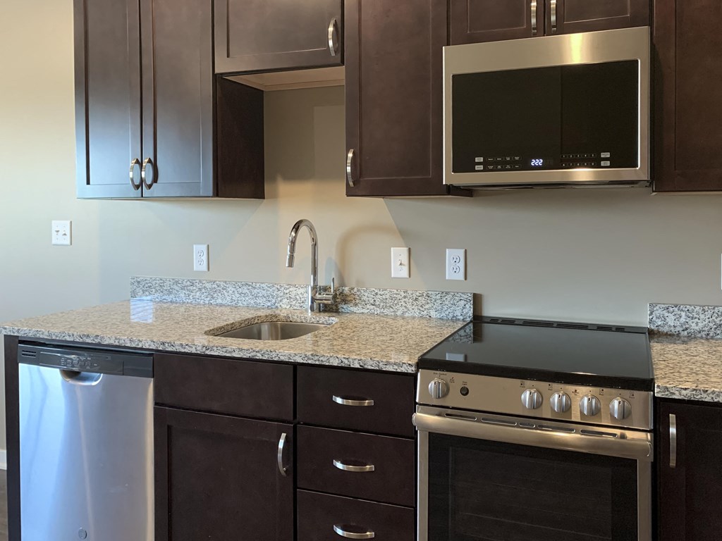 Kitchen with dark brown cabinets and matching stainless steel appliances in a studio apartment at the flats at shadow creek