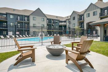 a firepit with Adirondack chairs around it in front of a gated pool area