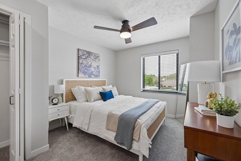 Bright apartment bedroom with ceiling fan and large window.