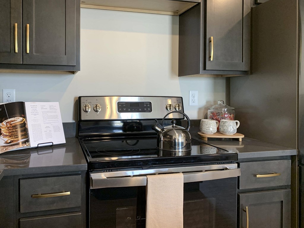 a kitchen with black cabinets with gold handles and stainless steel stove
