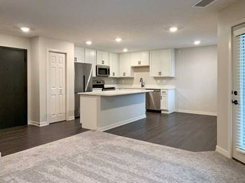 modern kitchen with white cabinets and a island with wood look flooring and carpet