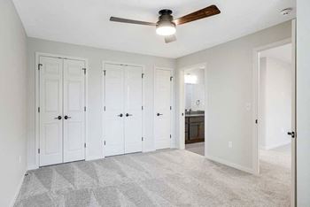 a bedroom with 3 closets, a ceiling fan, and a door to the attached bath