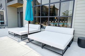 a patio space in front of a large window with two outdoor daybeds and an umbrella