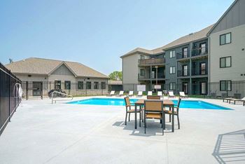 a swimming pool with a table and chairs in front of it and a row of lounge chairs behind it