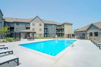 a resort style pool with lounge chairs surrounding it in the middle of an apartment courtyard
