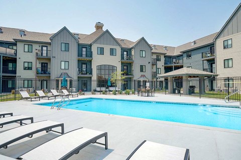 a swimming pool in the center of an apartment courtyard with lounge chairs next to it