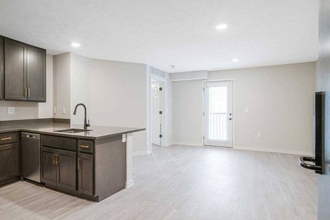 An empty living room and a kitchen with dark cabinets in the Dove at the Knock Apartments in Lincoln, NE