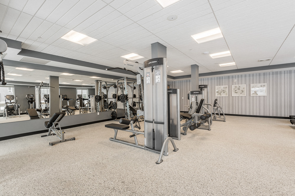 View of fitness center with weightlifting machines and mirrors at The Preserve apartments in Bloomington