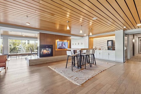 Community coffee lounge with a high-top table, bar stools, fireplace, and wood-paneled ceiling.
