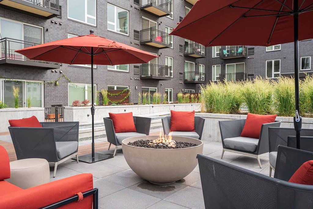 a patio with red couches and umbrellas around a fire pit in the zen garden