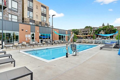 A large outdoor swimming pool surrounded by sun loungers and a building in the background.