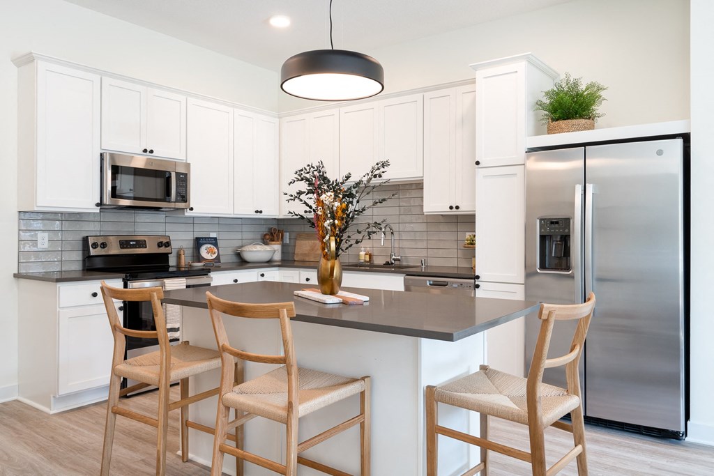 Kitchen with white cabinets and stainless steel appliances three wooden chairs surrounding kitchen island