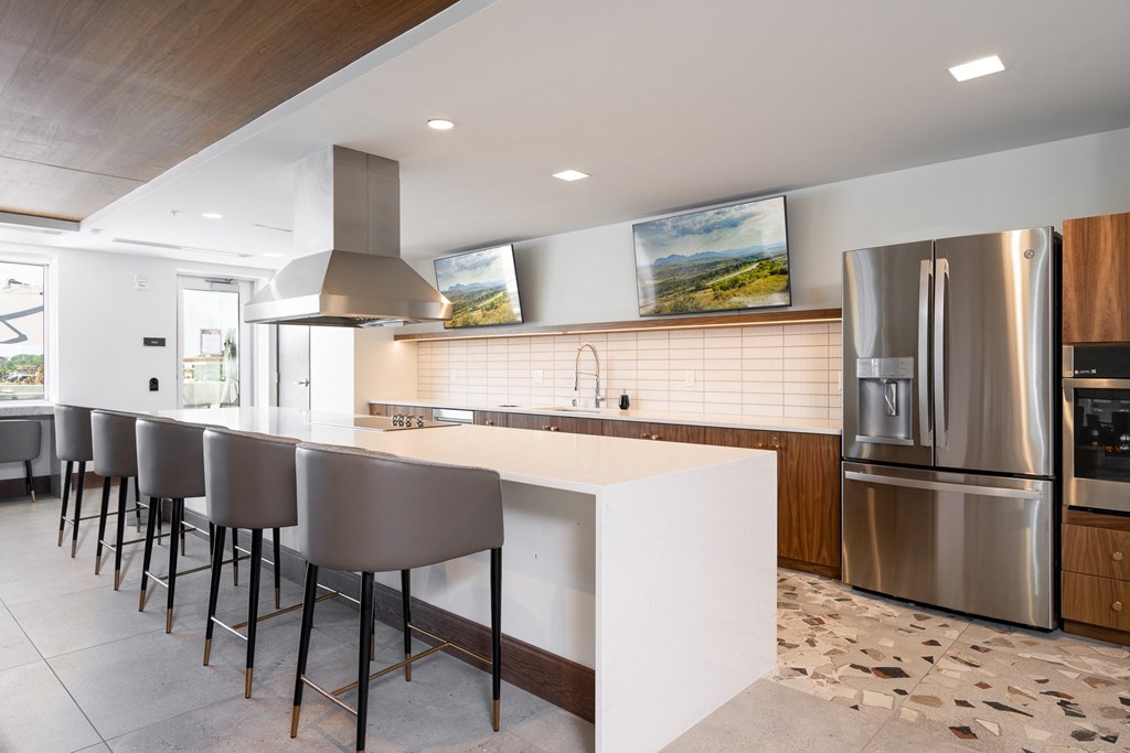 Community space kitchen with full stove, fridge, and oven. Large white countertop with barstool seating.